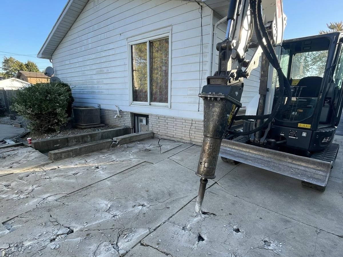 Excavator with breaker removing an old concrete slab